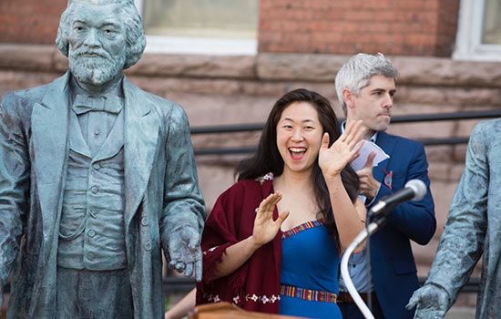 person waving next to her statue of Frederick Douglass.