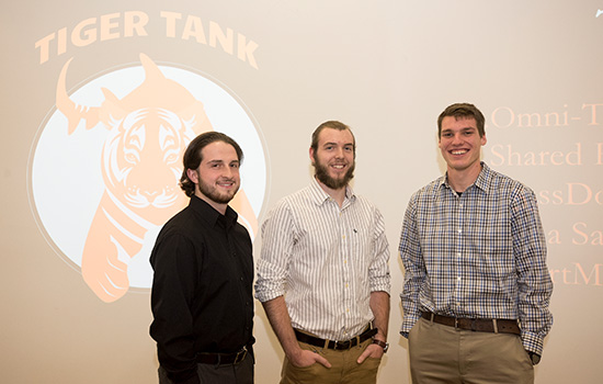 Three people in button down shirts standing in front of Tiger Tank logo.