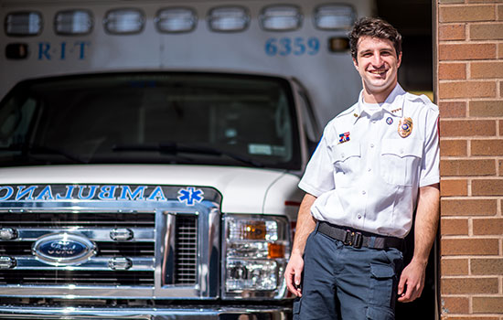 Oren Cohn poses for a photo in his RIT Ambulance uniform in front of one of the ambulance vehicles.