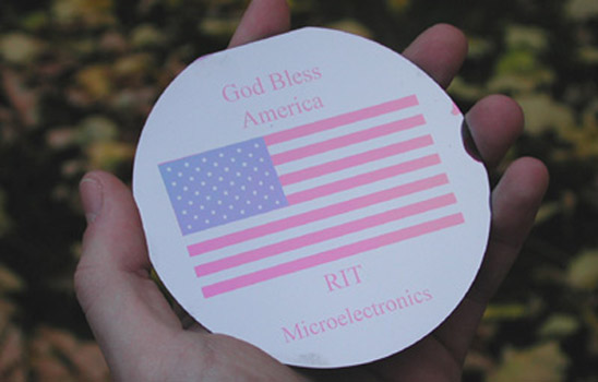 hand holding computer wafer imprinted with American flag and the words God Bless America.