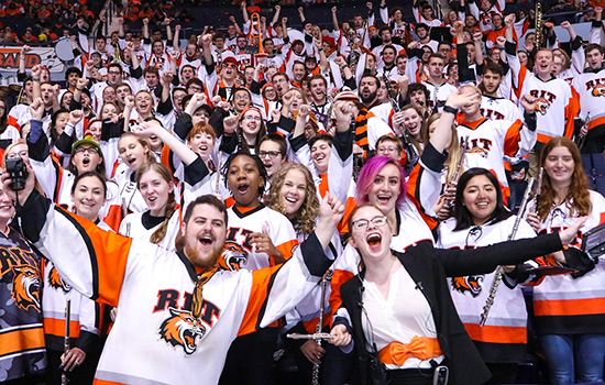 RIT pep band in matching RIT Jerseys pose for picture at hockey game.