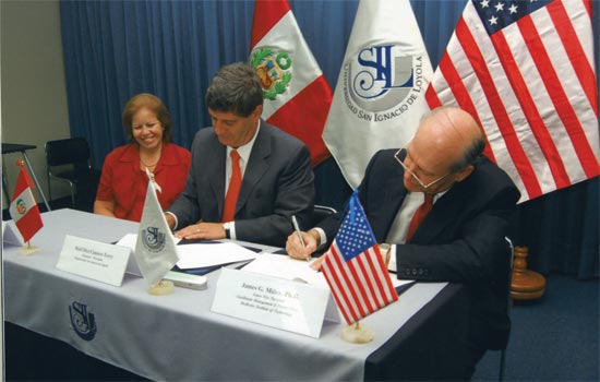 People signing documents in front of flags