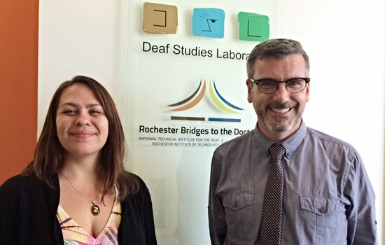 Two people posing in front of "Deaf Studies Laboratory" sign