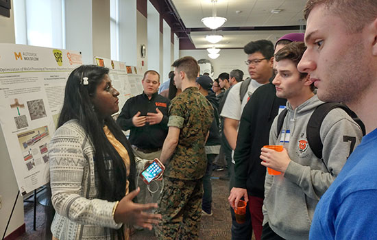 Shalomin Thomas explains her research to a group of students at a poster session.