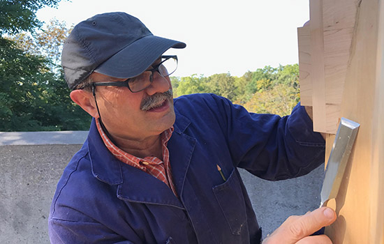 man scraping a piece of wood with a chisel.