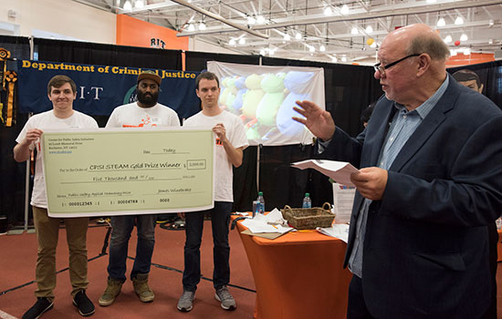 Three Clockwyse team members hold up a large check while the CPSI director talks to a crowd about their first-prize accomplishment.