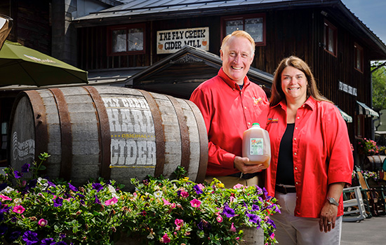 Bill and Brenda Michaels pose next to the entrance of their Cider Mill, holding a jug of their cider.