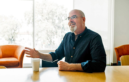 John Butler sitting at a table with a cup of coffee.