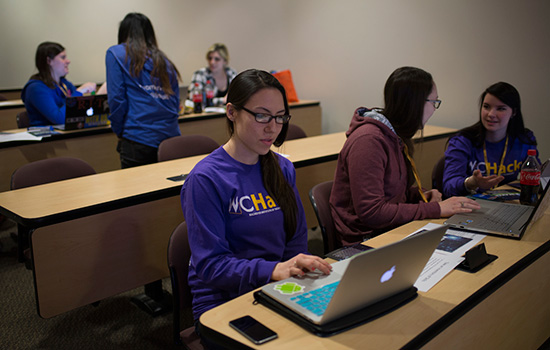 women at desks wearing matching purple women in computing shirts.
