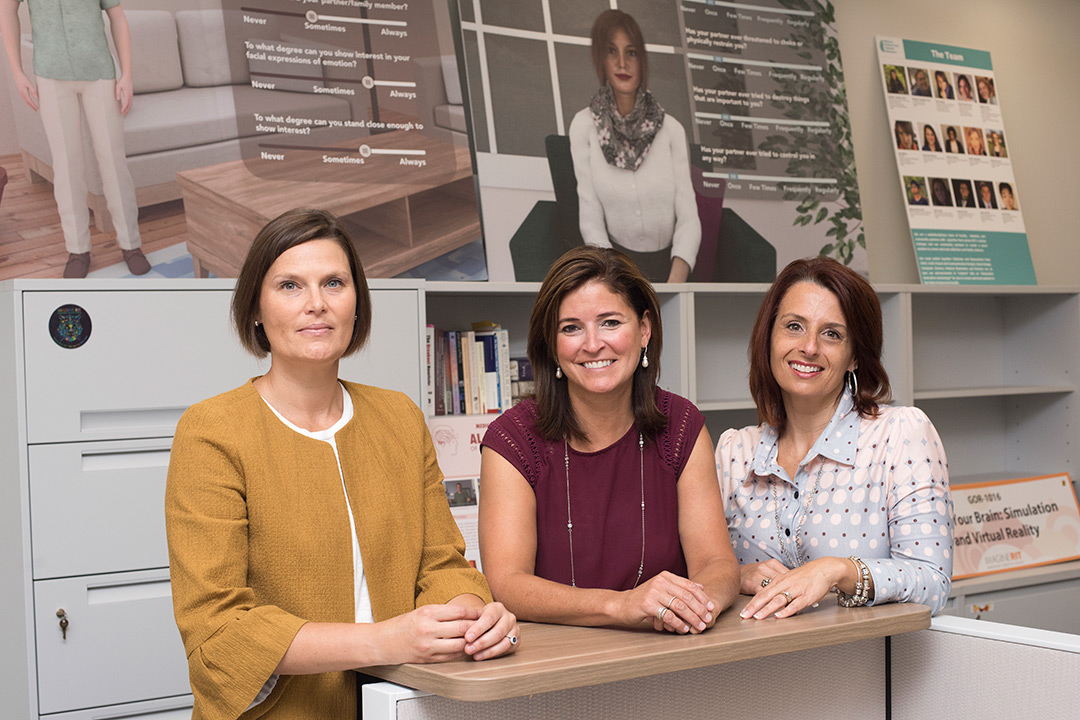 Three women stand and pose for a photo in an office setting.