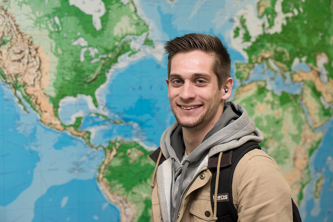 Connor Draughn poses for a photo and smiles in front of a large world map.