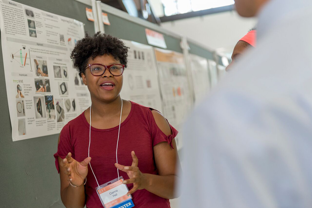 Cianna Dresden Hall excitedly explains her research to onlookers, talking with her hands and smiling as she speaks.