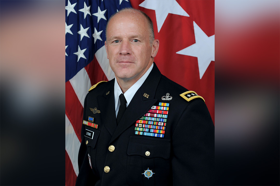 Man in decorated military uniform with American flag in background