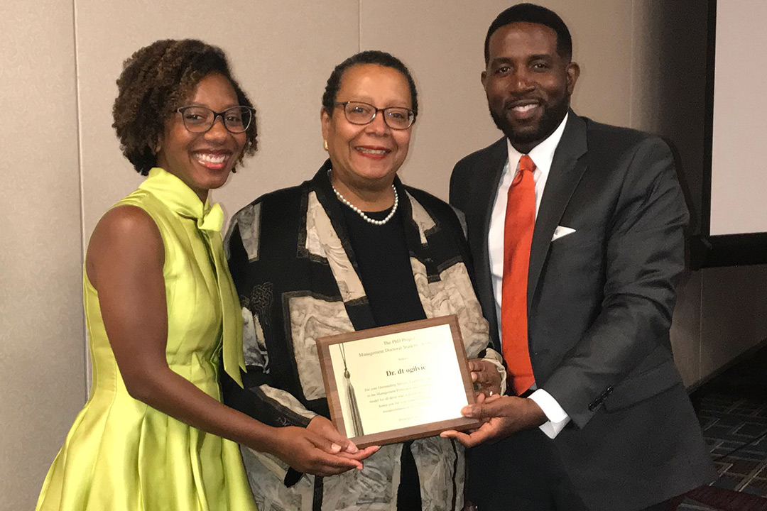 Three people pose for a photo holding dt ogilvie's, center, plaque she received for the Trailblazer Award.