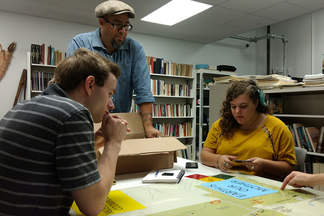 Jordana Deutsch and Matthew Hough sit at a table and look over designs with Michael Galban.