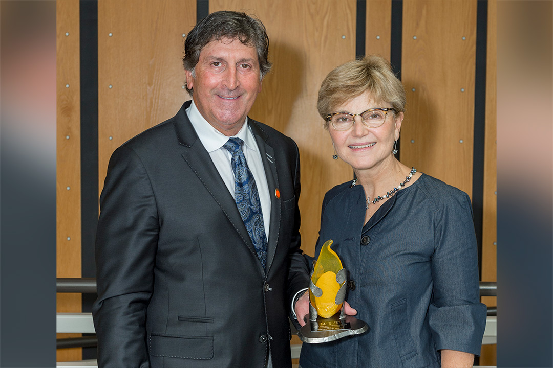 Steve Wear and Sophia Maggelakis pose for a photo together, Wear holding the distinguished alumni award trophy.