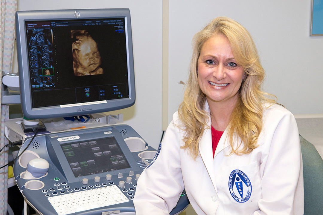 Lisa Allen poses with an ultrasound screen. The screen shows a high-quality ultrasound image of a human baby.