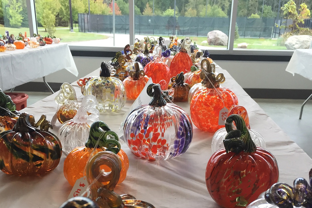 Various styles and colors of class pumpkins laid out on a white tablecloth. 