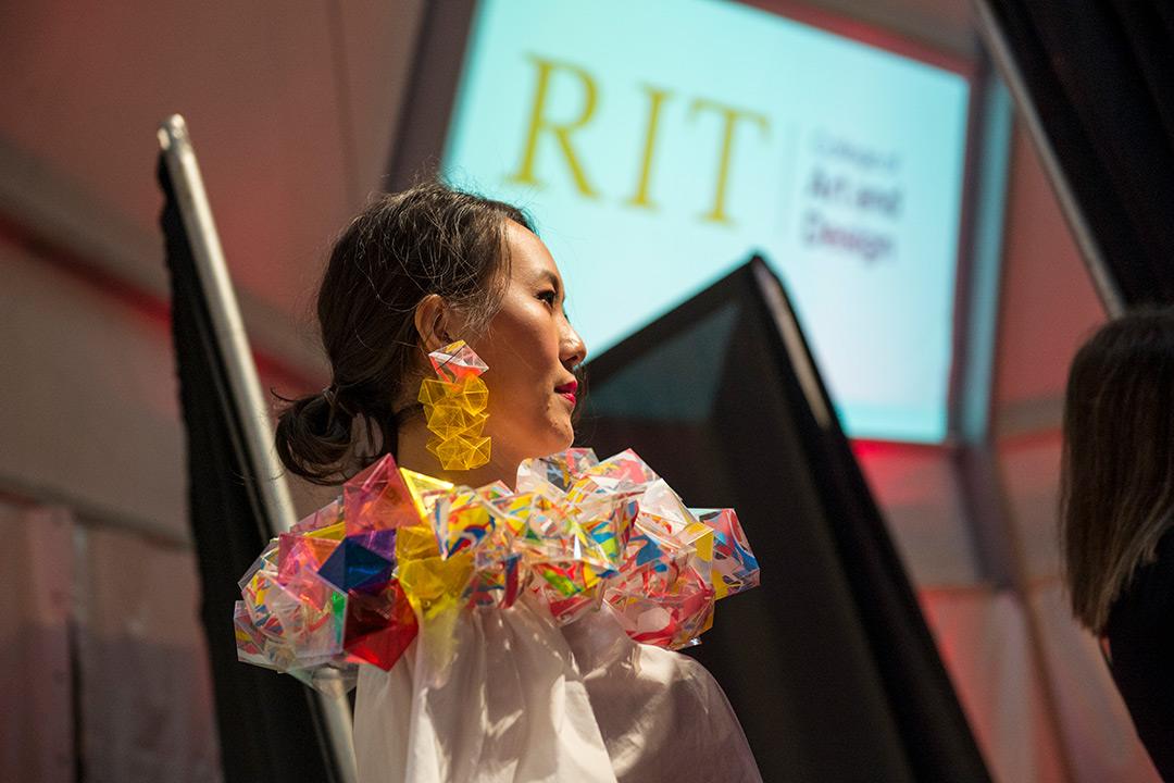 A model dressed in a white dress and colorful, 3D geometric collar and matching 3D geometric earrings.