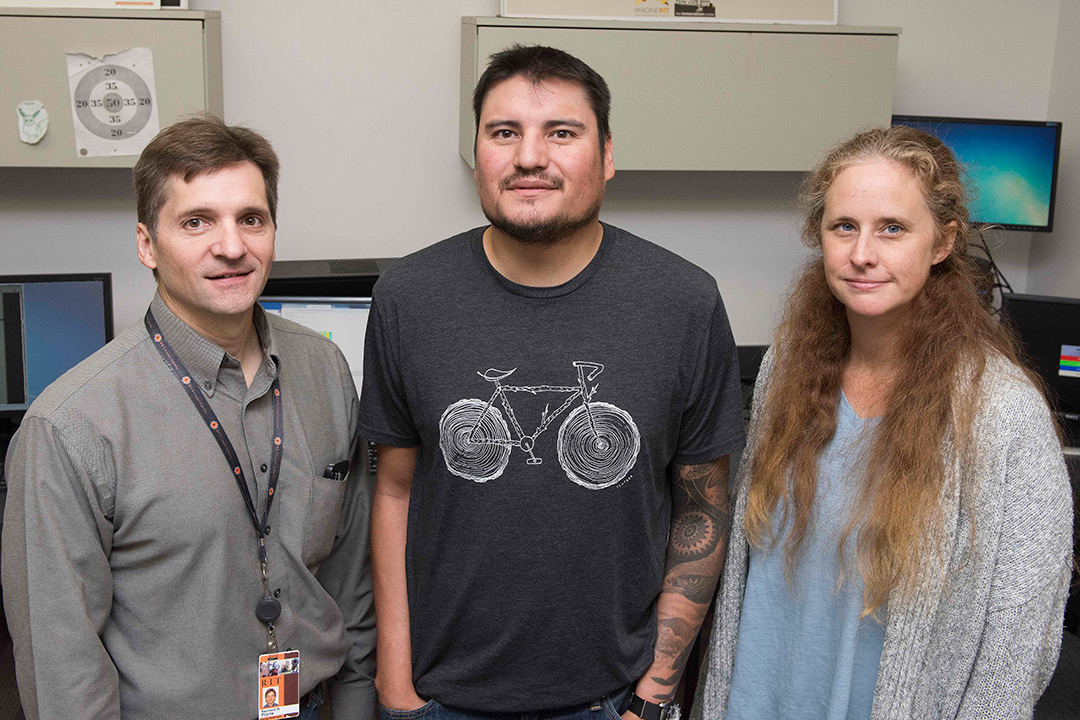 A group of three researchers stand together in a line and smile at the camera.