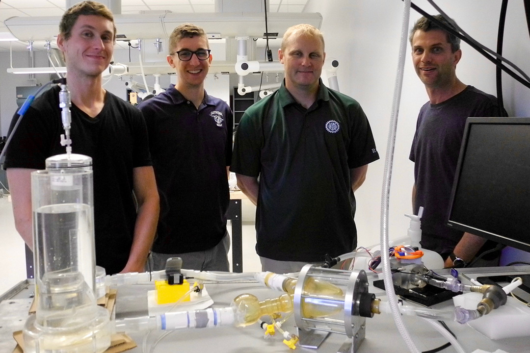 Two students and two faculty members working on this project pose for a photo in front of their lab bench, which is covered in different tools and models.