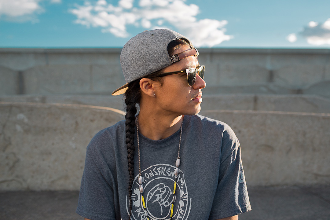 A side profile of Frank Waln looking off camera to the right. He is wearing a backward gray and brown baseball hat and a gray teeshirt.