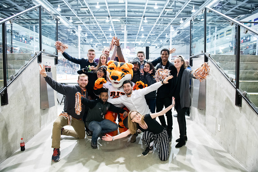 Group of students pose with tiger mascot at entrance to hockey stadium.