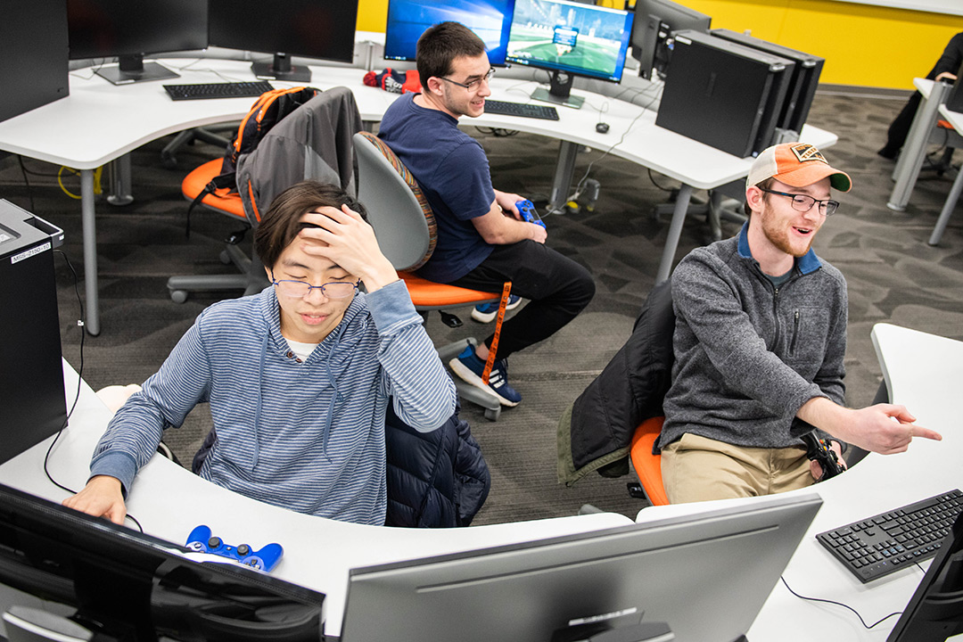 three students sit at computers at half-circle tables