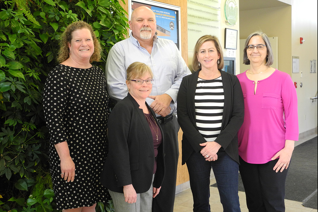 Group of faculty members stand near wall of plants