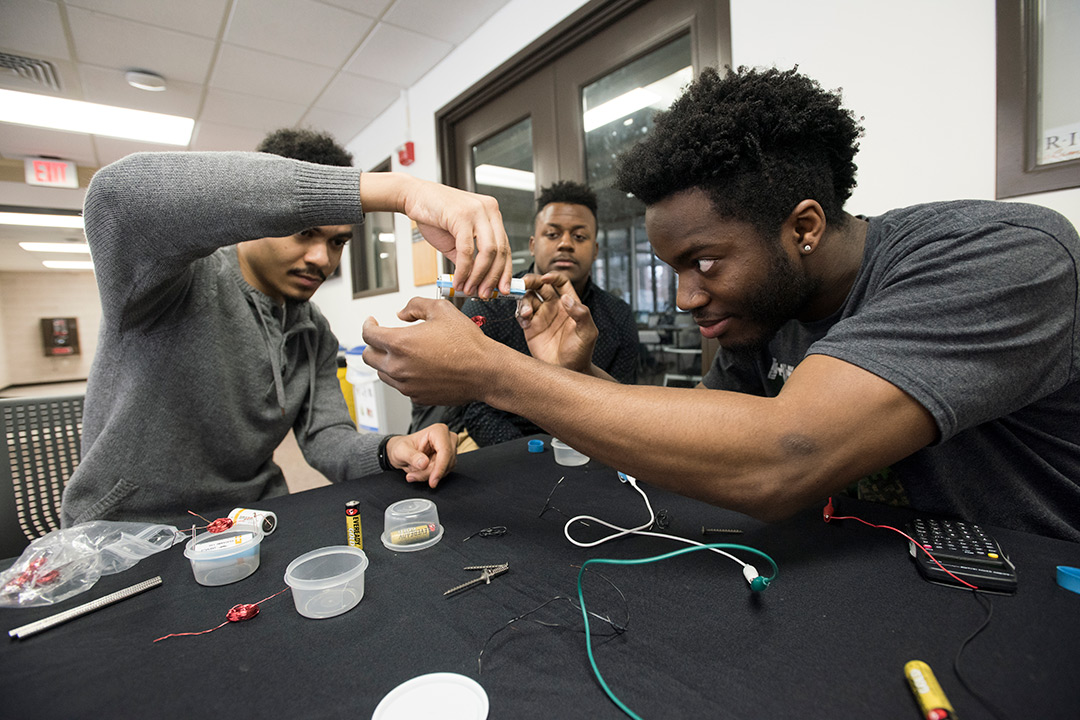 three students demonstrate how to make a simple motor using everyday materials