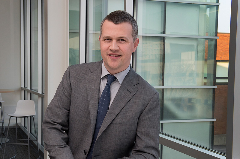 Professor in gray suit stands near window