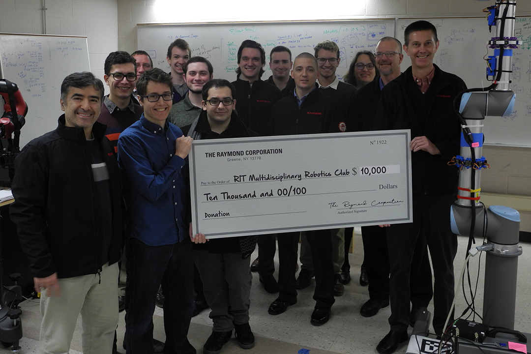 Group of students and professors stands holding giant check for $10,000 from the Raymond Corporation