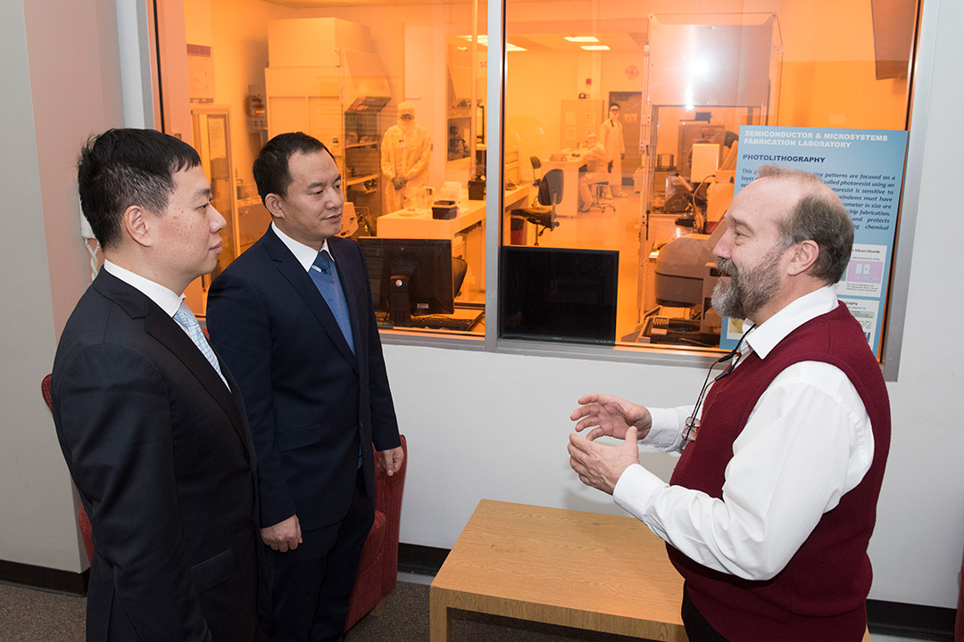 Three men talk outside of cleanroom lab