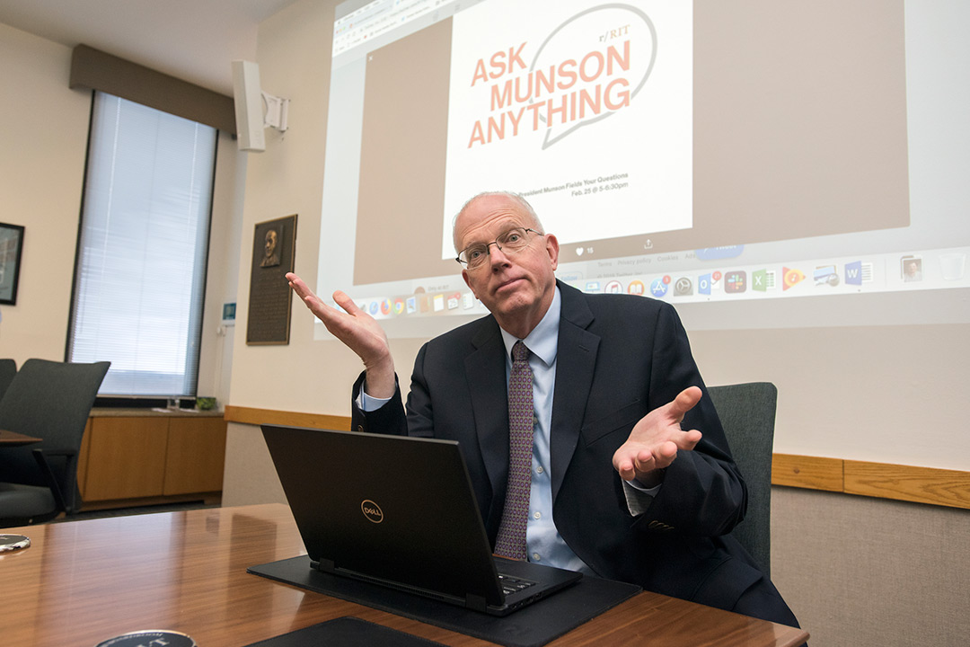 Man in suit sits at table with laptop and projector screen behind him reads: Ask Munson Anything