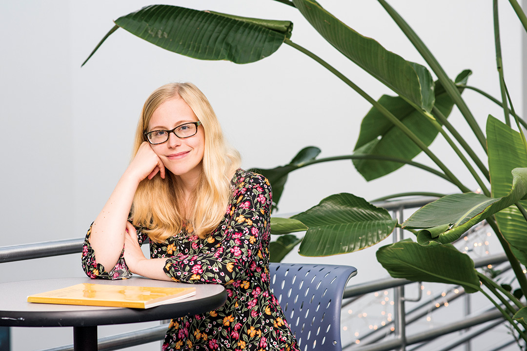 Woman wearing glasses and floral print dress sits at table.