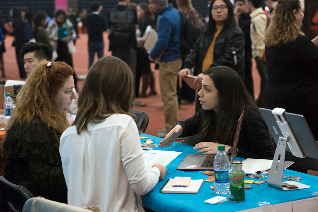 Student sits at table talking to company reps in career-fair setting