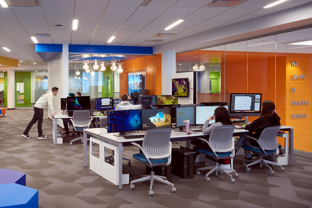 Students work on desktop computers in open room with glass walls