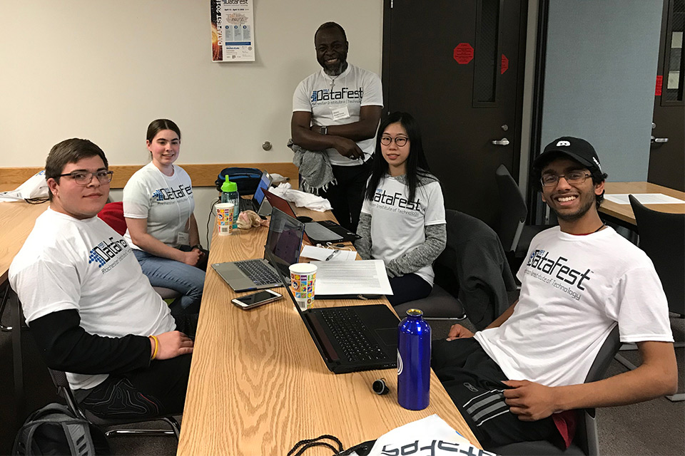 Group of five students and professor sit around table wearing T-shirts that read: DataFest