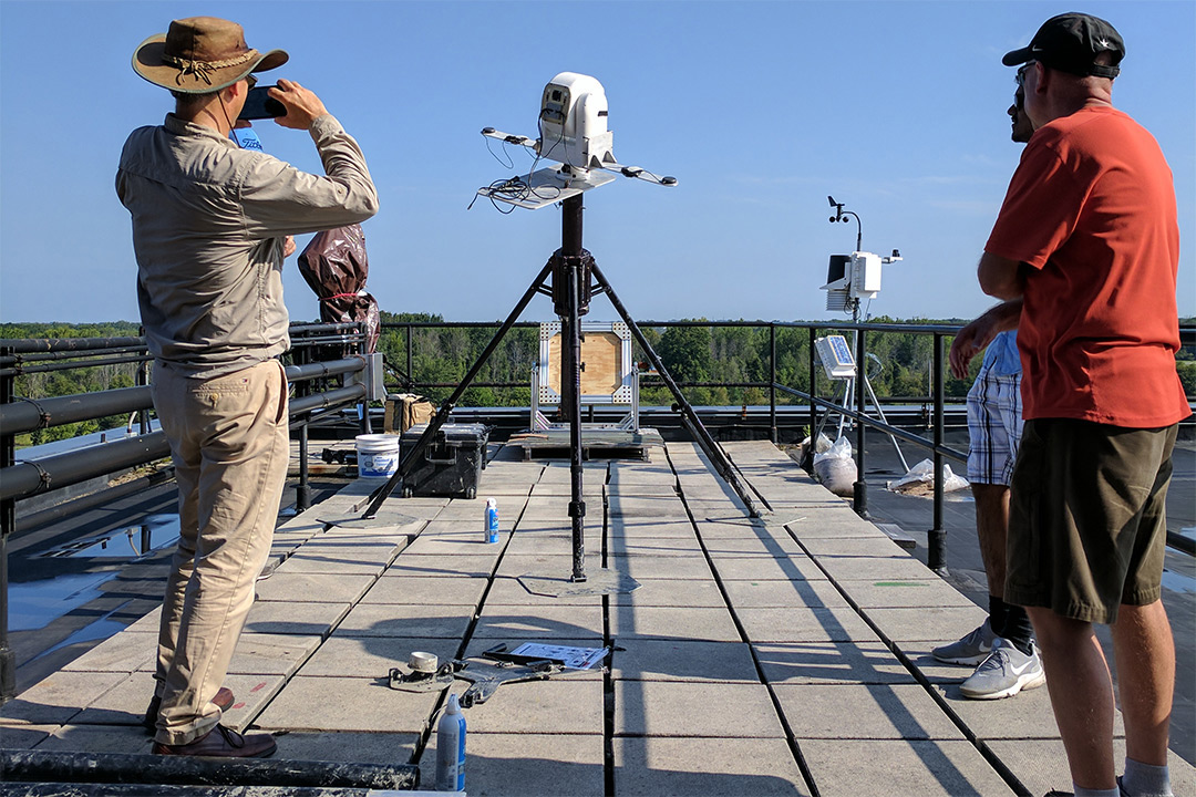 Three researcher watch hyperspectral camera on roof.