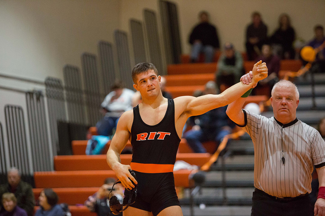 Student in wrestling singlet stand with ref raising his arm in the air