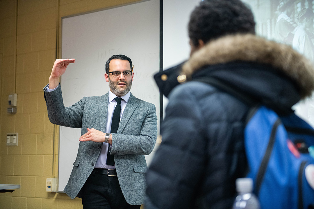 Back of student in foreground as professor speaks in background.