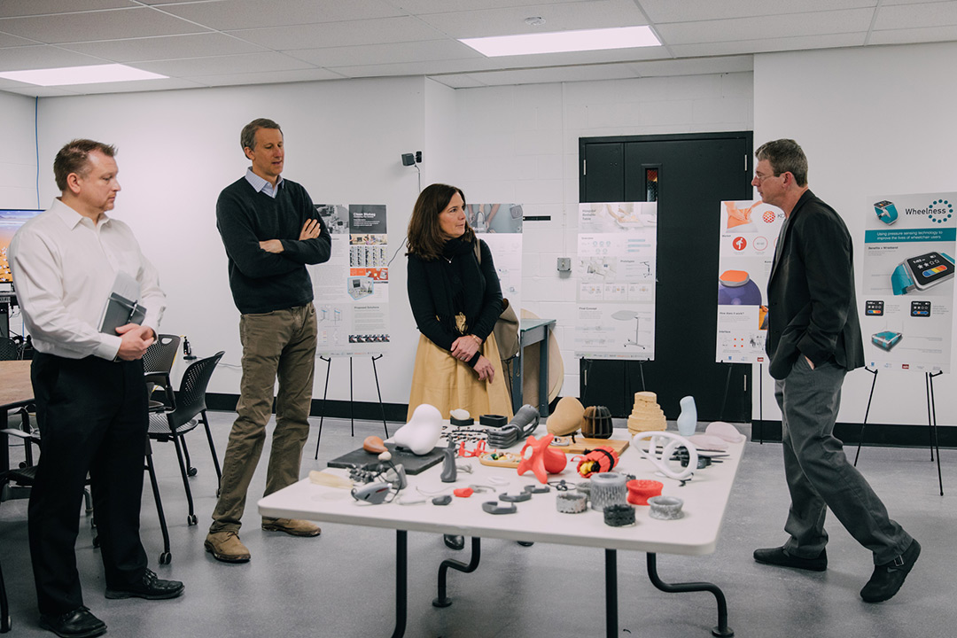 Professor and three company reps stand around table with 3D-printed gadgets