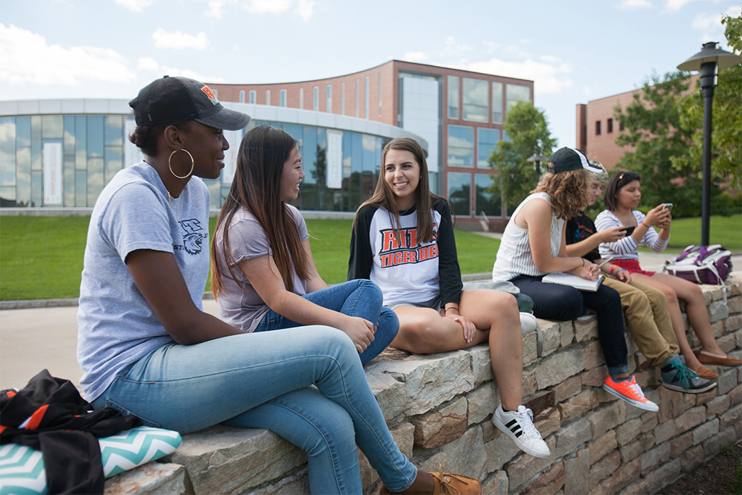 Six students sit on rock wall.