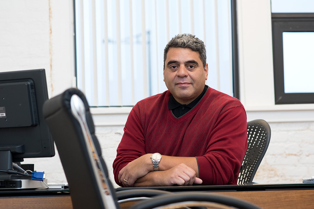 Man wearing red sweater sits at desk.