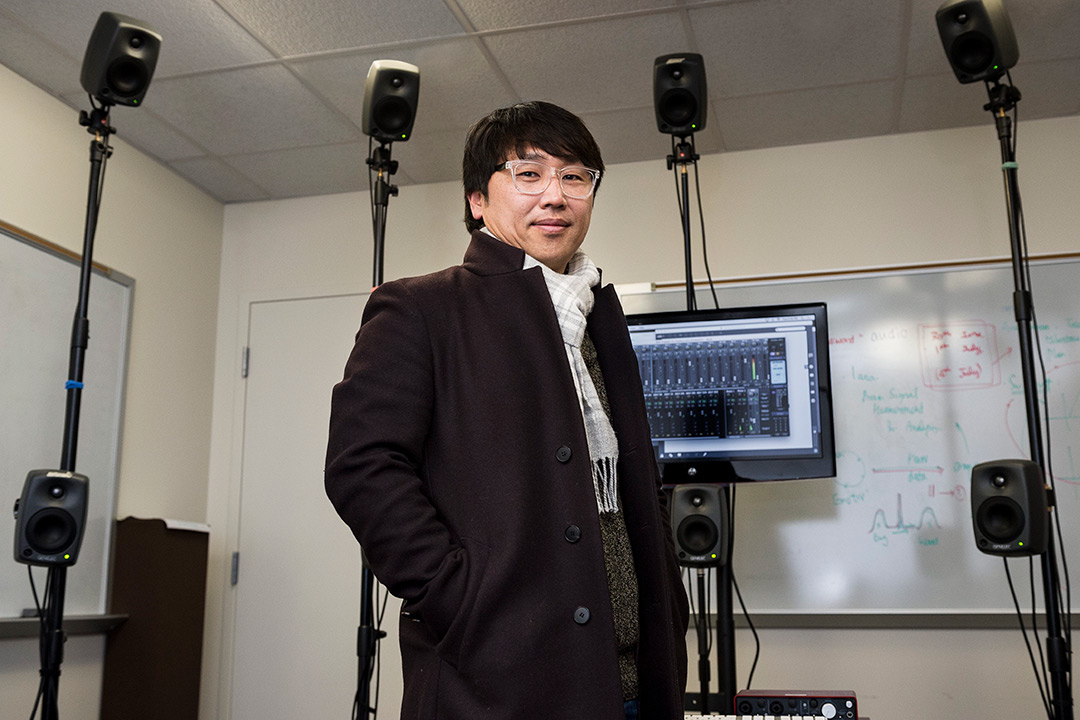 Researcher stands in front of TV screen surrounded by small speakers