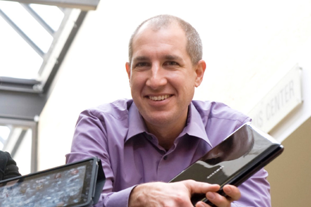 Head-and-shoulders view of professor holding a closed laptop