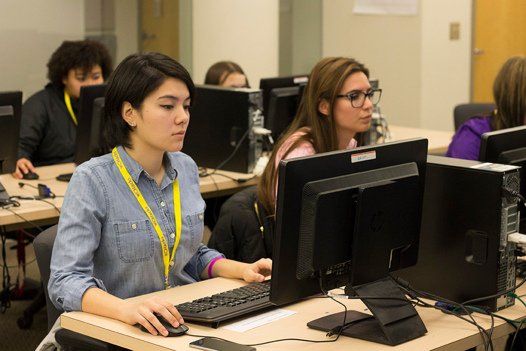 Two women sit at table with desktop computer