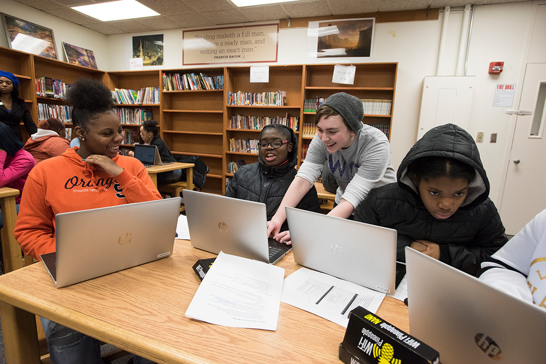 Three high school students and one RIT student sit around table working on laptops