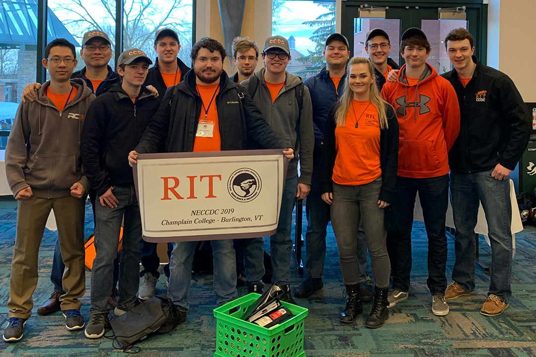 Group of students holds banner that reads: RIT NECCDC 2019, Champlain College - Burlington, VT