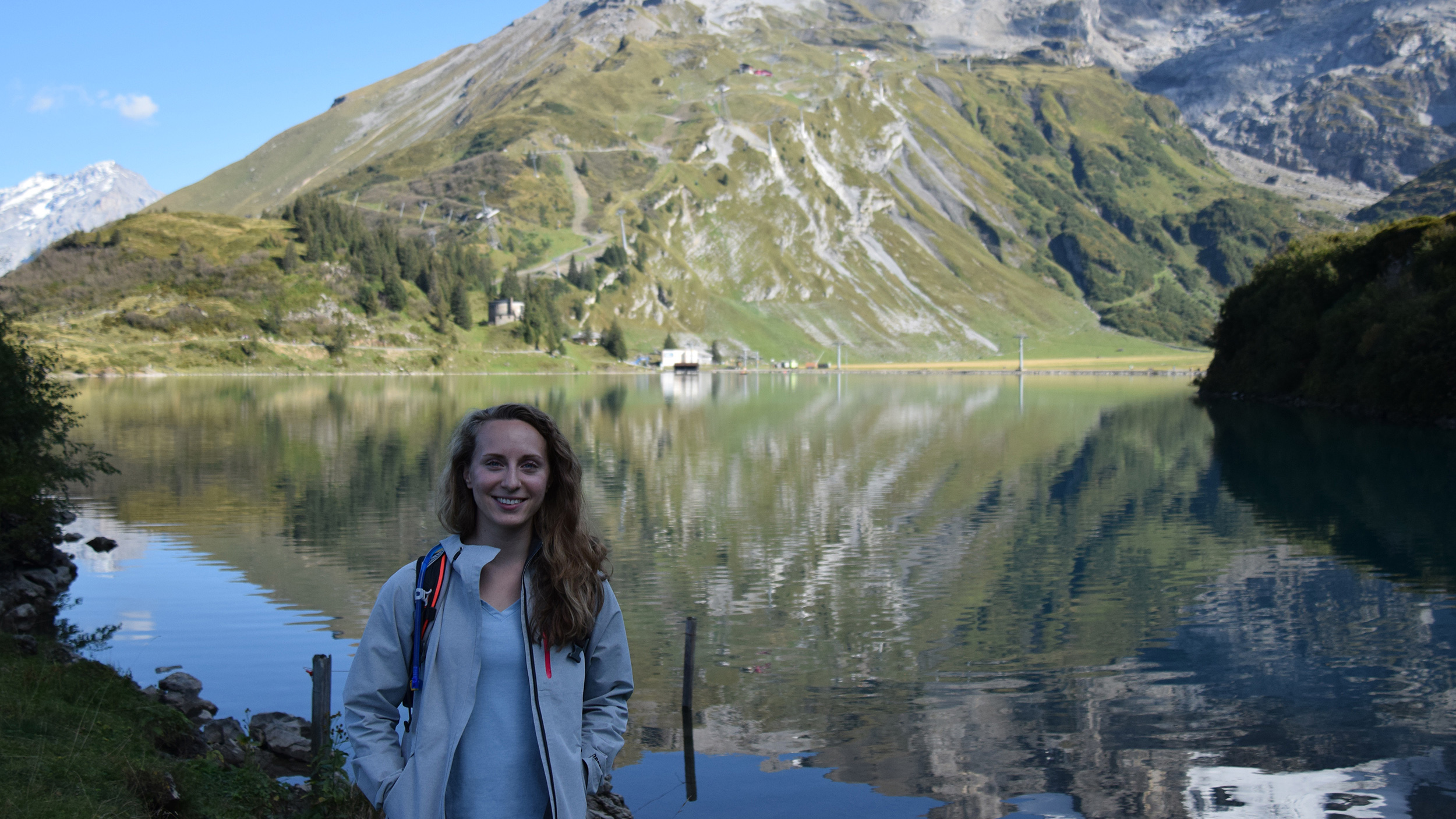 Scholl posing in front of lake with large mountains behind her